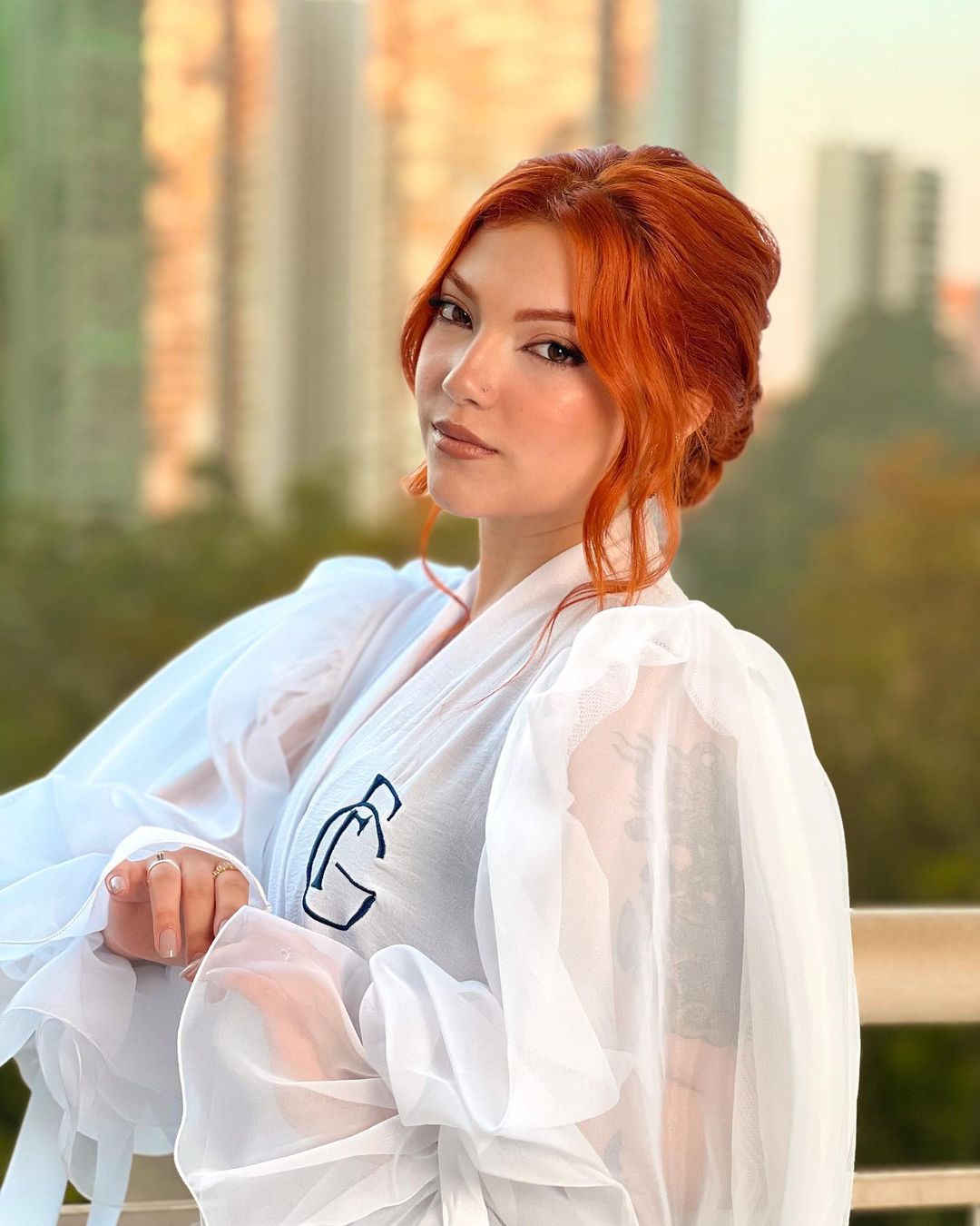 A confident individual with vibrant red hair posing in a breezy white robe